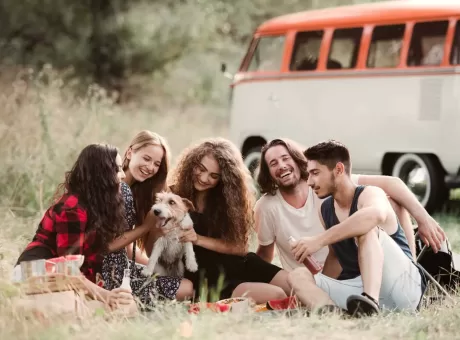 a-group-of-young-friends-with-a-dog-sitting-on-grass-on-a-roadtrip-through-countryside-.webp